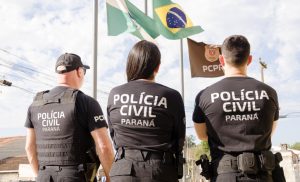 Grupo de candidatos da PC treinando juntos com edital impresso e plataforma de estudos aberta no notebook