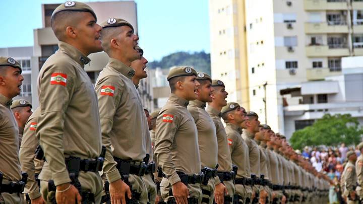 Mesa de escritório com contrato de concurso da PMSC assinado e carimbo oficial ao lado de símbolos de estudo
